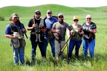 Six hunters in blaze orange and camo standing together in a green rolling-hills field at the 2022 Veterans Upland Bird Hunt