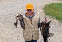Second group photo of youth hunters and mentors posing in front of sponsor banners with their pheasant harvest at the 2022 Youth Mentor Hunt