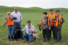 Teenage boy in a baseball cap and grey hoodie holding two harvested pheasants on a gravel road at the 2022 Youth Mentor Hunt