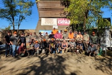 Large group of veterans, first responders, and chapter members posing in front of a barn with event signage at the 2023 Veterans and First Responders Hunt