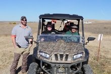 Hunter standing beside a camouflage UTV with two passengers in the rolling-hills field at the 2023 Veterans and First Responders Hunt