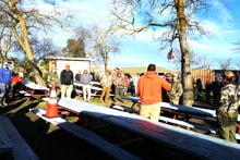 Group of hunters gathered around picnic benches under bare trees for a pre- or post-hunt briefing at the 2024 R3 Upland Bird Hunt