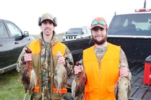 Two hunters in blaze orange jackets standing in a parking area holding multiple harvested pheasants at the 2024 R3 Upland Bird Hunt
