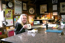 Woman with long blonde hair smiling behind a counter in a rustic shop filled with hunting and dog memorabilia at the 2024 Women's Upland Bird Hunt