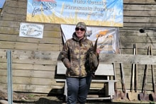Woman in camo jacket standing in front of the Pheasants Forever Yolo County chapter sign and bench at the 2024 Women's Upland Bird Hunt