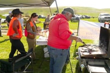 Hunters gathered around a grill at an outdoor event under a canopy