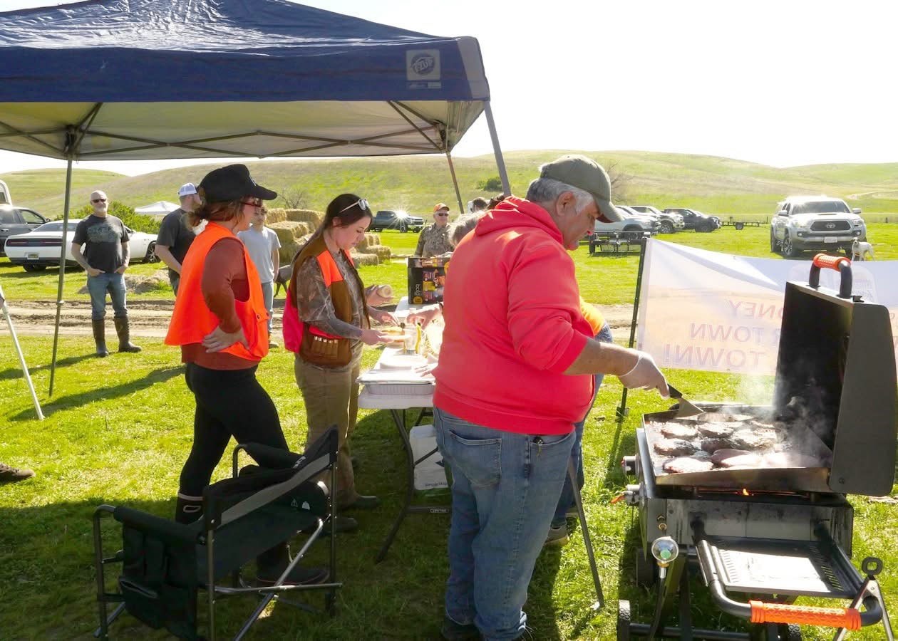 Hunters gathered under a canopy tent around a flat-top grill cooking at an outdoor event