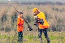 Group of youth hunters and mentors walking through a field with a dog