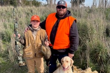 Two hunters in orange vests walking through a field together