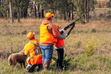 Youth hunter and mentor walking together through a field carrying a shotgun